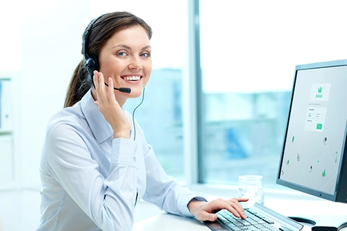 Une femme, gestionnaire de flotte devant son ordinateur et répondant via son casque à un appel téléphonique.