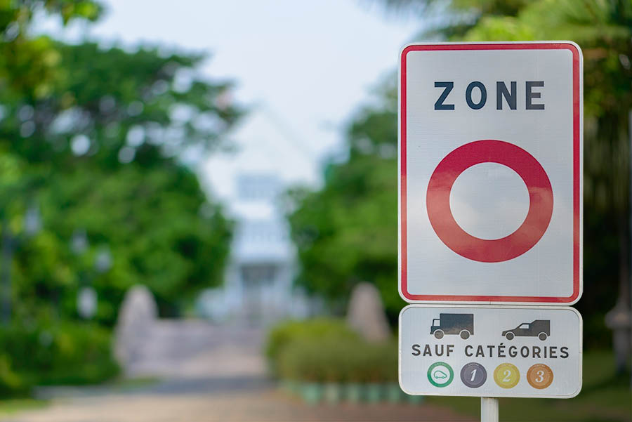 Photo de ville avec un panneau d'entrée de zone ZFE avec vignette Crit'Air autorisée 1, 2, 3 et véhicule électrique
